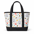 Cotton tote bag with bee print on a light background and black polka dot straps and base, featuring a structured trapezoid shape and front exterior pocket.