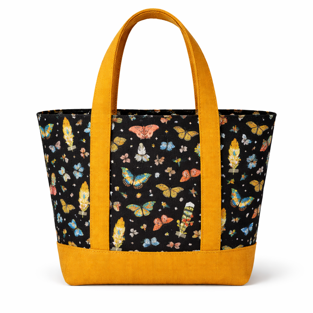 Cotton tote bag with black butterfly print and mustard yellow straps and base, featuring a structured trapezoid shape and front exterior pocket.