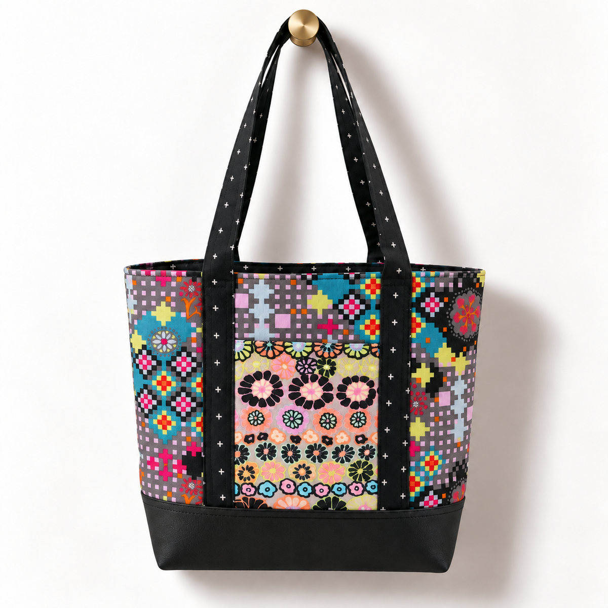 Handmade cotton tote bag with retro pixel floral pattern and black cross detail straps hanging on a gold knob