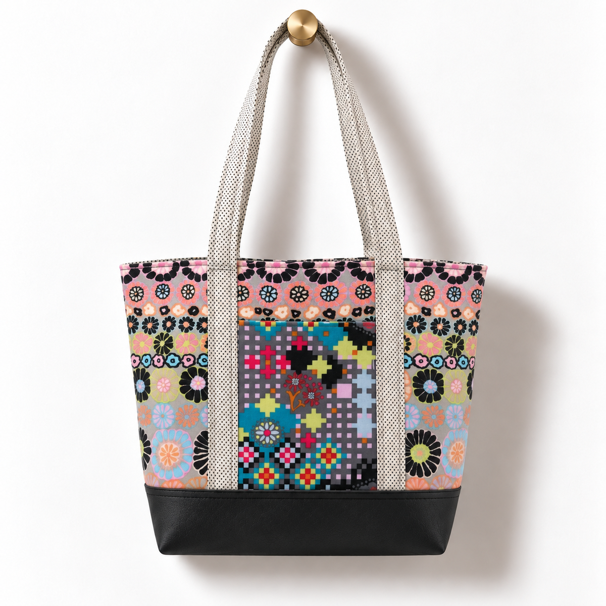 Handmade cotton tote bag with pastel floral mosaic pattern and cream micro dot straps hanging on a gold knob