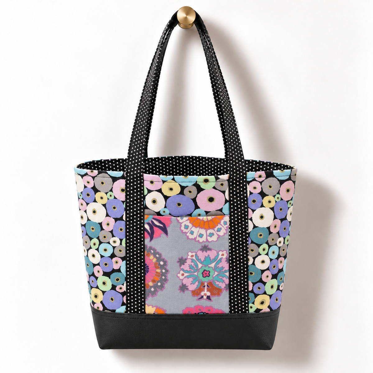 Handmade cotton tote bag with mod floral ring pattern and black and white dotted straps hanging on a gold knob
