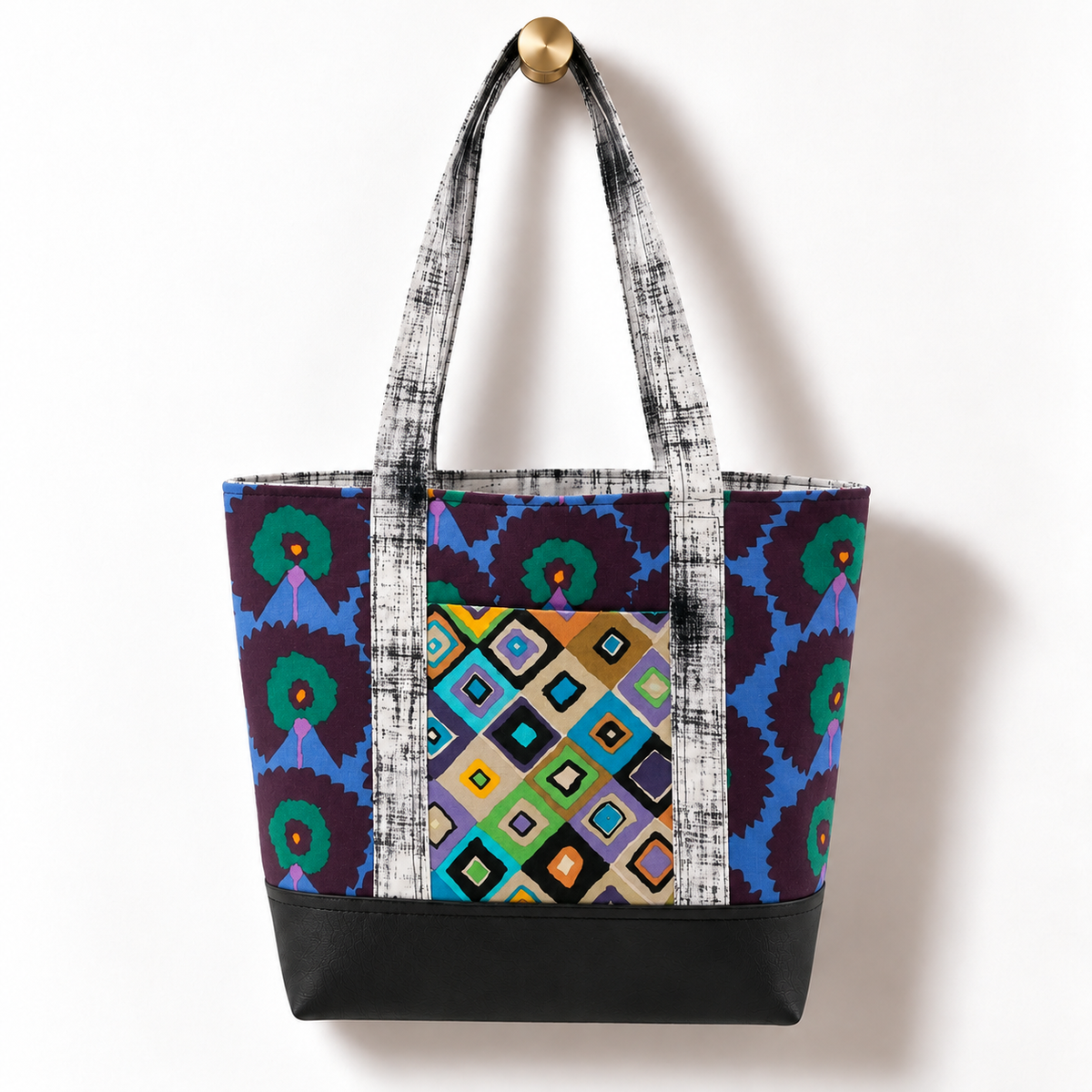 Handmade cotton tote bag with peacock floral pattern and textured black and white straps hanging on a gold knob