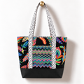 Handmade cotton tote bag with colorful tropical feather pattern and white dotted straps hanging on a gold knob