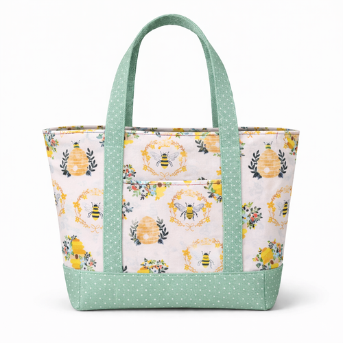 otton tote bag with bee and floral print on a light background and sage green polka dot straps and base, featuring a structured shape and front exterior pocket