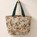 multicolor trailing tiny floral print on cream, dark forest-green handles, tan lining weekender tote hanging on a gold knob