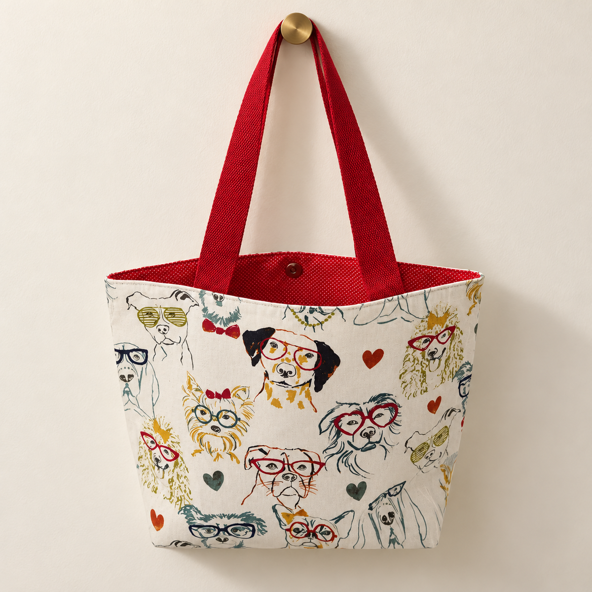 dogs wearing colorful eyeglasses and hearts on cream, red handles, red lining with tiny white dots weekender tote hanging on a gold knob