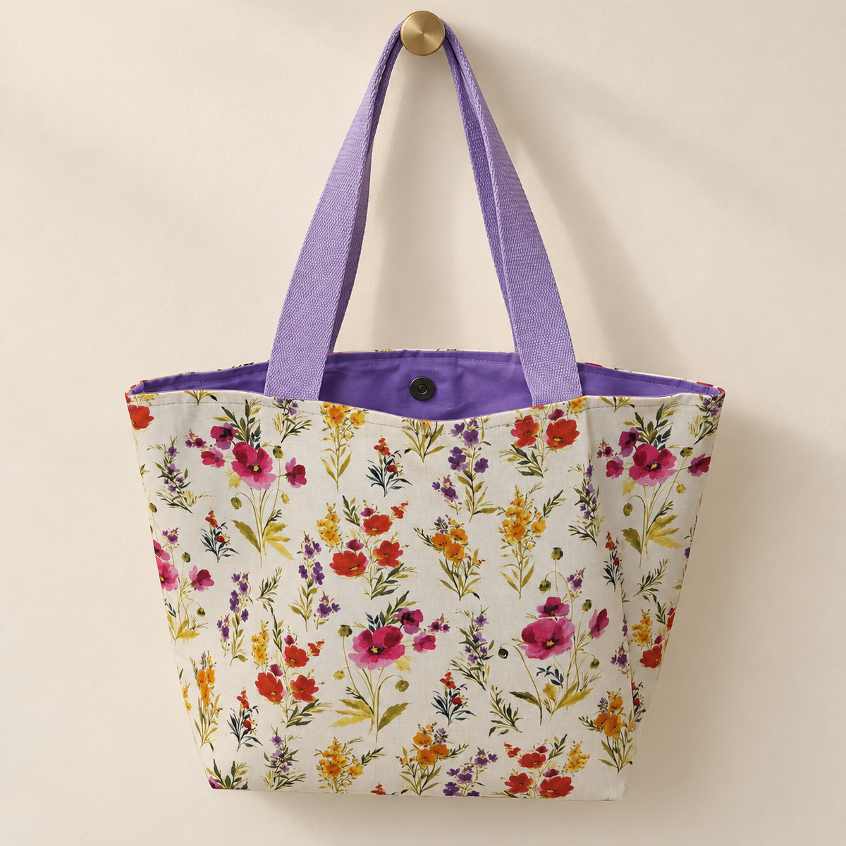 upright meadow flower sprigs on pale cream, lavender handles, purple lining weekender tote hanging on a gold knob