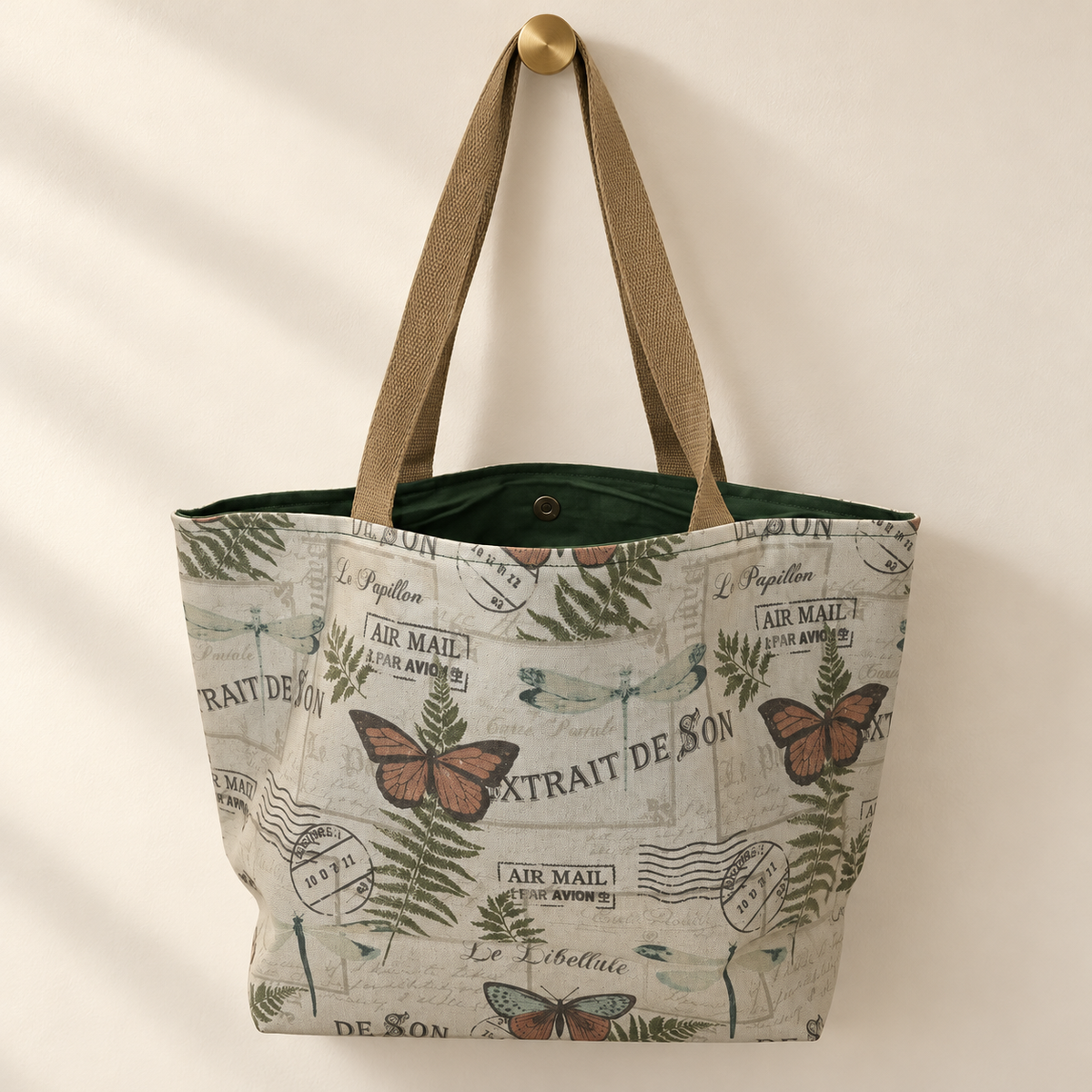 same vintage butterfly dragonfly fern French postcard print, tan handles, dark forest-green lining weekender tote hanging on a gold knob